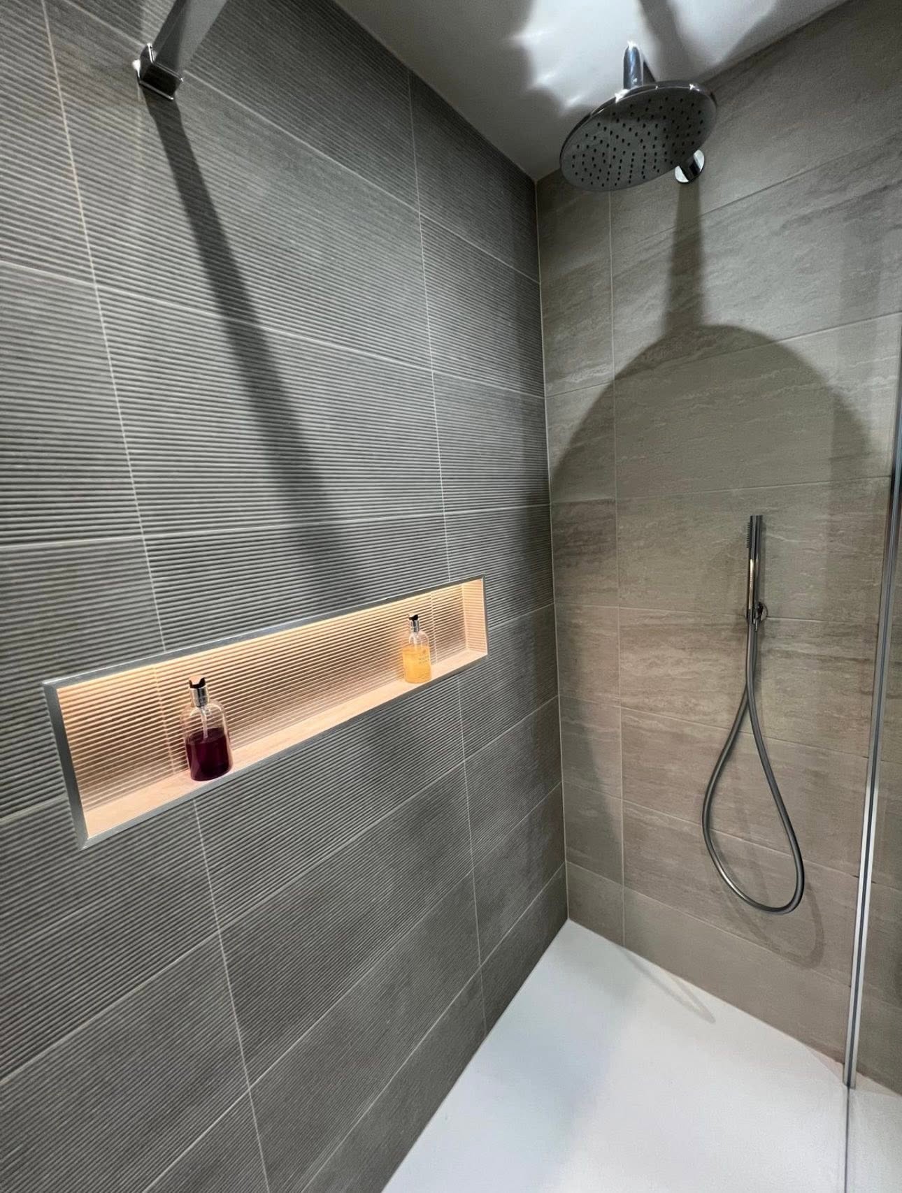 Shower detail with ceiling mounted rain head, ribbed grey tiling and illuminated recessed shampoo niche